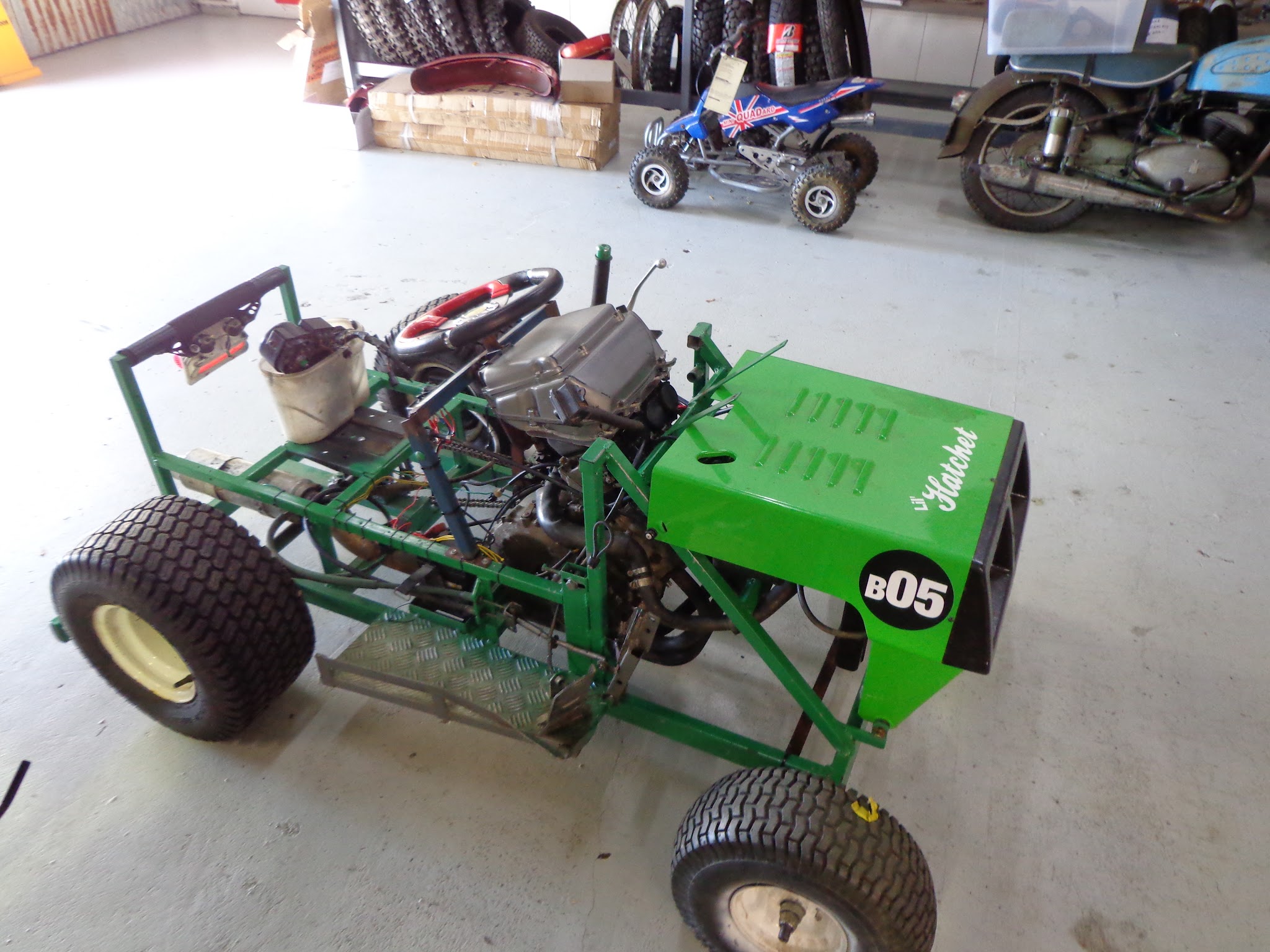 A green home built ride-on mower racer badged Li'l Hatchet, with a mini quad behind it