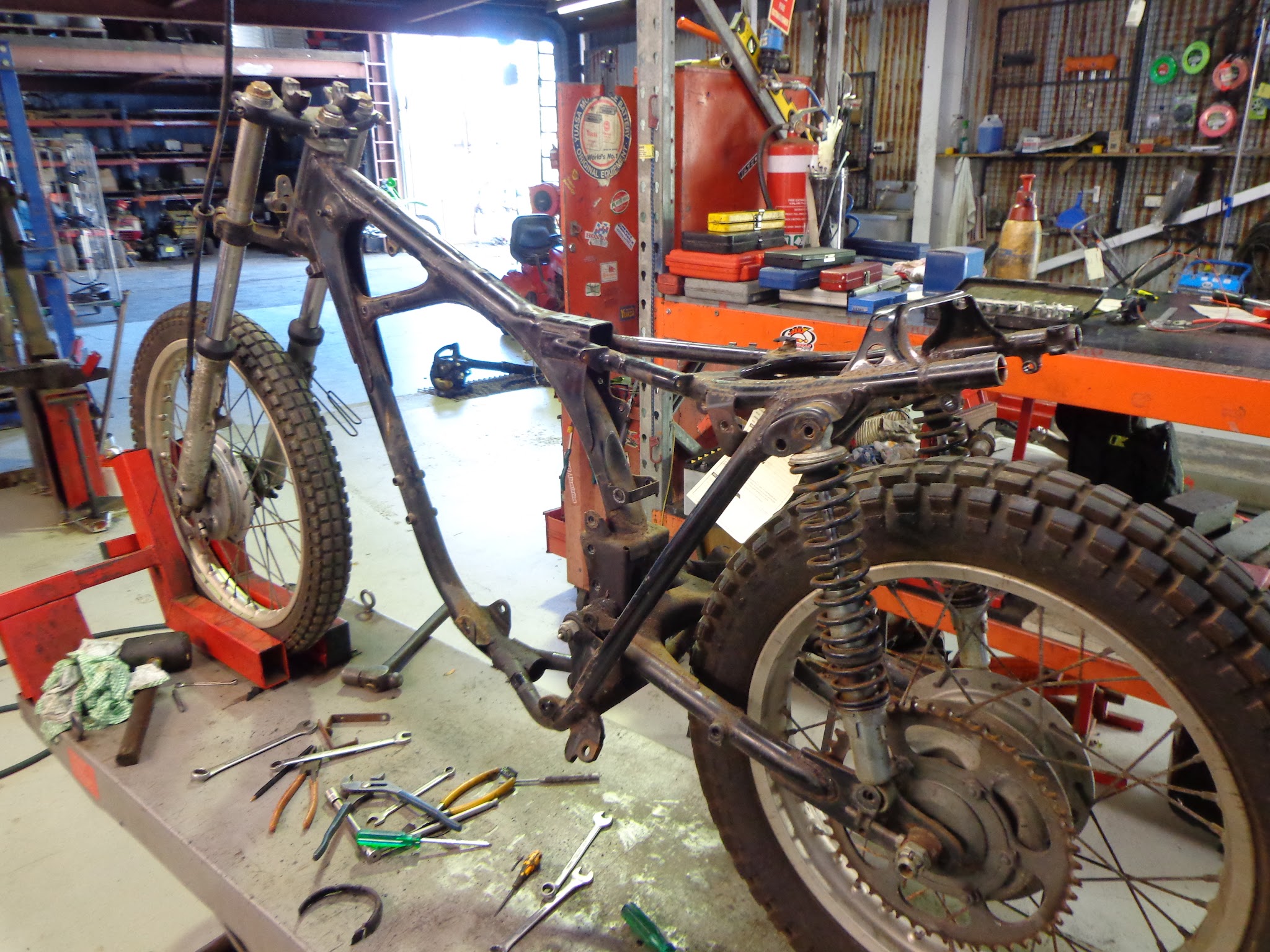 A motorcycle stripped back to a bare rolling chassis on the workshop bench, with spanners and screwdrivers laid out around it