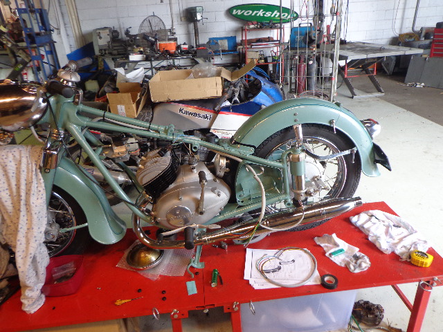A mint green vintage motorcycle part way through a rebuild on a red lift table